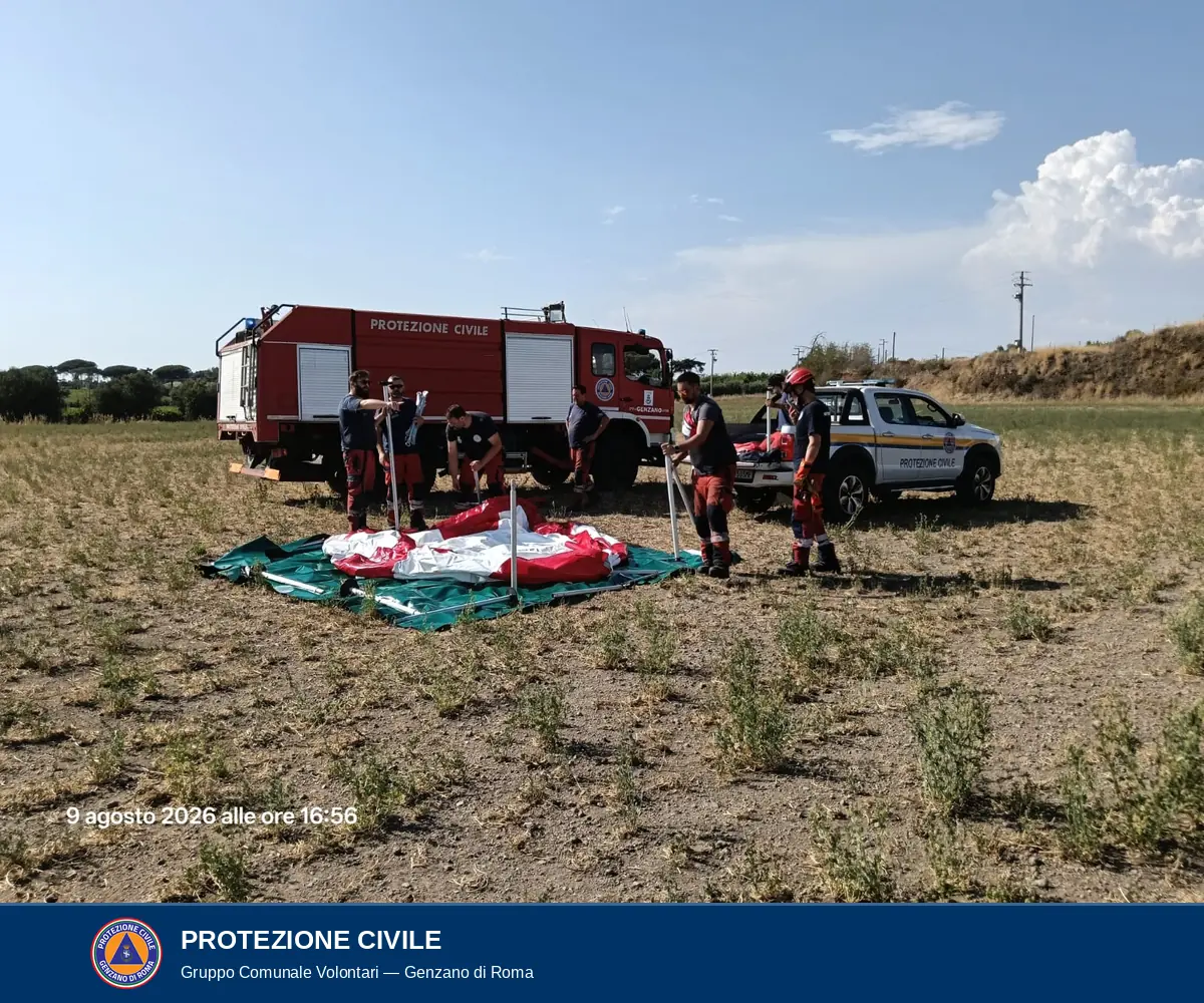Volontari con in mano i tubolari metallici del telaio della vasca, davanti all'autocarro antincendio rosso e a un pick-up bianco della Protezione Civile.