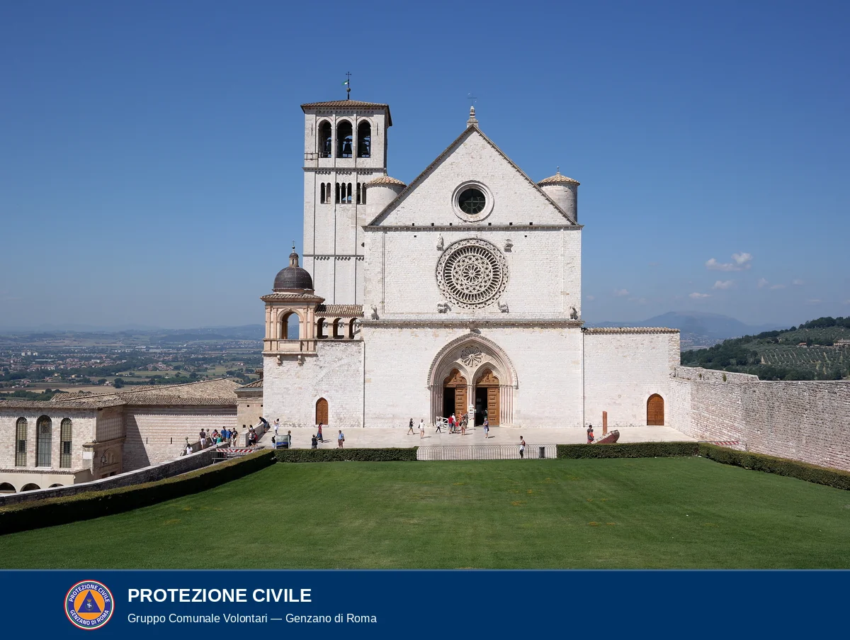Facciata della Basilica Superiore di San Francesco d'Assisi in stile gotico, in pietra bianca, con rosone centrale, portale a doppio arco e campanile romanico sulla sinistra; cielo azzurro terso e prato verde in primo piano