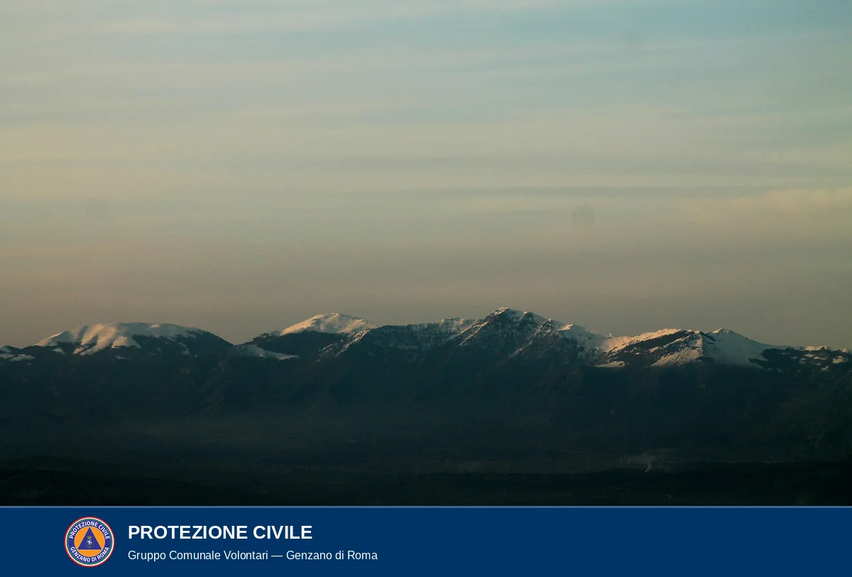 Foto a colori delle vette innevate del Massiccio del Pollino, creste rocciose scure con neve residua nelle vallecole, controluce al tramonto